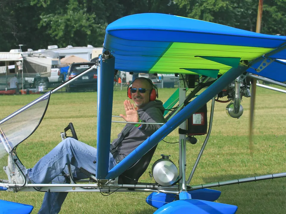 Blue and green Aerolite 103 ultralight with its pilot on the field at Oshkosh