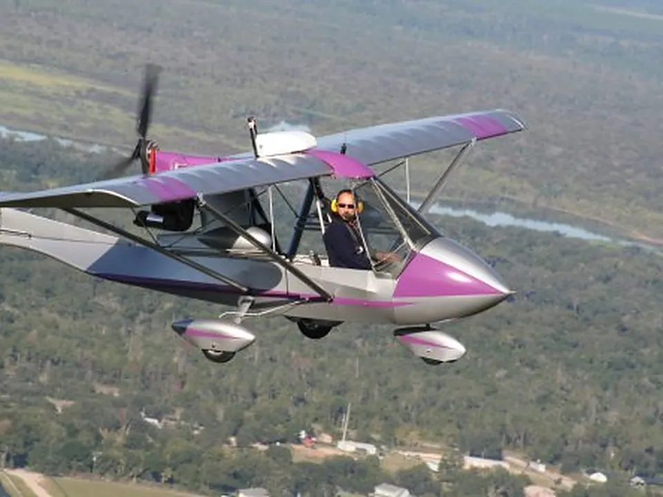 Purple and white Challenger with cargo pods flying over green fields