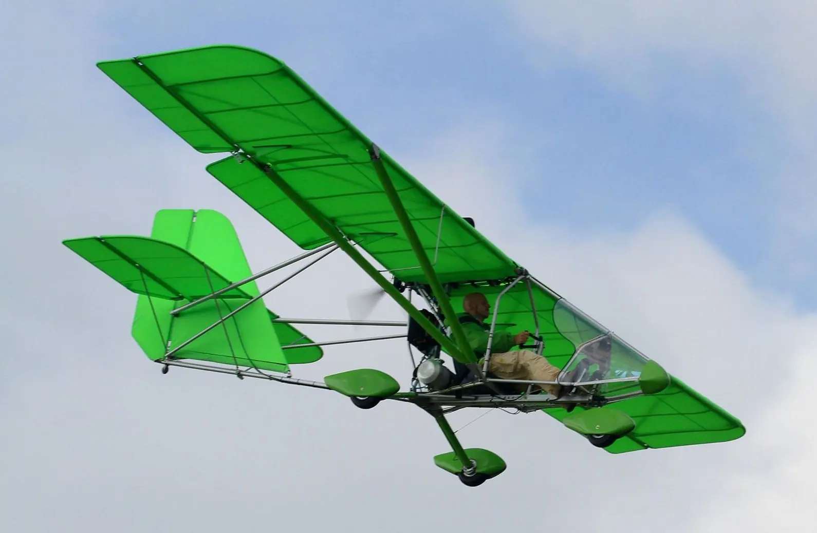 A green and white Aerolite 103 ultralight in flight against a clear sky
