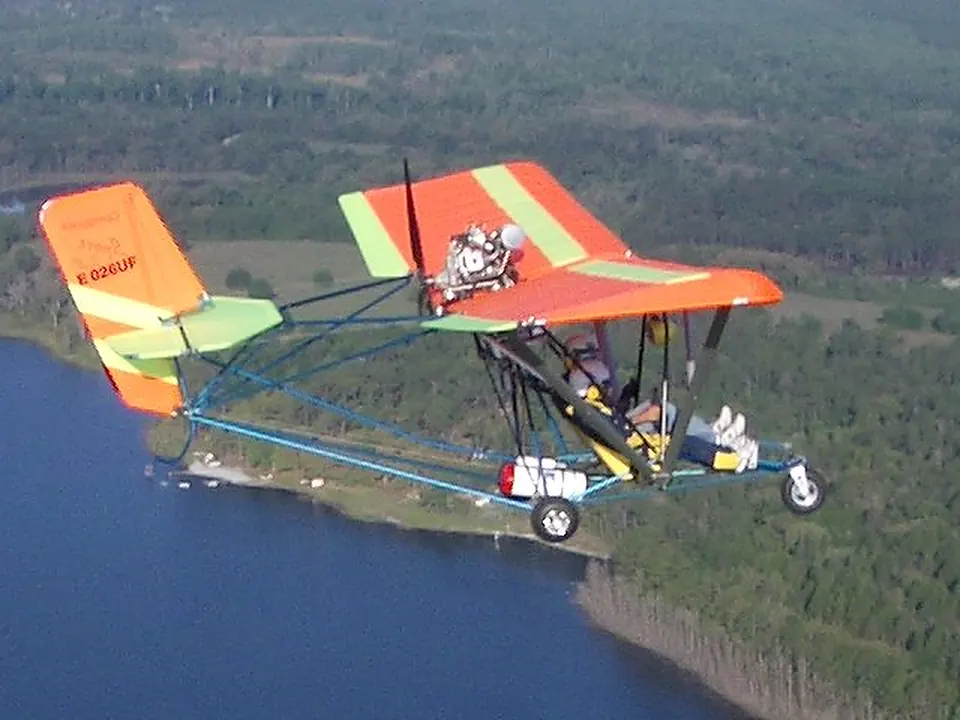 Orange and white Quicksilver Sport 2S flying low over a lake